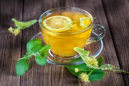 A cup of medicinal, lime tea, standing on a wooden table, surrounded by fragrant linden flowers, in the rays of sunlight.の写真素材