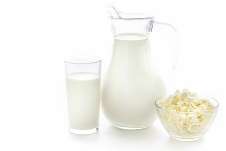 Cow milk in a glass jug and cup in a next to a plate of fresh cottage cheese on white background. Healthy food for people.の写真素材