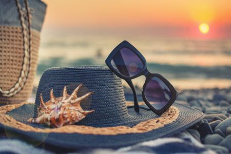 Weekend on the beach by the sea.Summer women's beach accessories for your sea holiday: straw hat, sunglasses, beach bag and striped towel, seashell.の写真素材