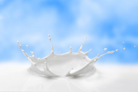 Milky splash against the blue sky with gentle clouds. Splash of milk in the form of a milk crown.の写真素材