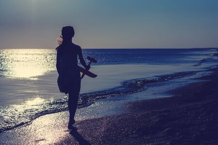 Silhouette of a girl with a toy airplane in her hand against the backdrop of a shining ocean at sunrrise.の写真素材