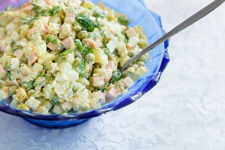 Russian salad with olive mayonnaise in a blue plate, on a white tablecloth.の写真素材