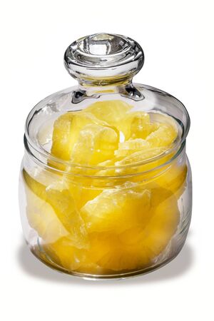 Dried pineapple candy rings, in powdered sugar, close-up under sunlight, lying in a transparent glass jar, on a white background.の写真素材