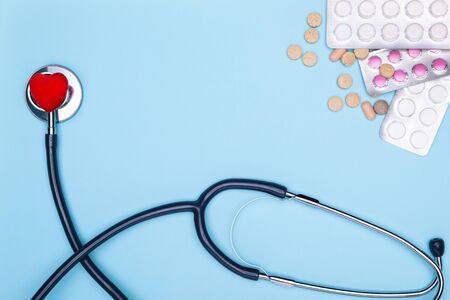 Blue background lies a statoscope, a red saddle and pills. Closeup of painted heart, lot of drugs and stethoscope on blue background.の写真素材