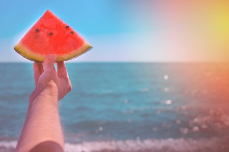 Watermelon, juicy slice in the hands of a woman with over the sea, in the rays of a sunny sunset. Diet of tropical fruits.の写真素材