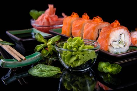 Japanese food. A set of various rolls of salmon, eel, shrimp and red caviar, in a beautiful green bowl, on a black background with reflection.の写真素材