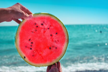 Round watermelon, juicy slice in the form of the sun, in the hands of a woman against the sea, in the rays of sunlight. Diet of tropical fruits.
の写真素材