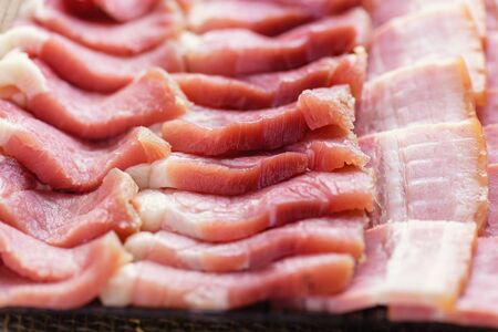 Bacon slices close-up. Fresh cooked food. Fresh cold sliced bacon on the background of natural linen fabric. Raw chopped bacon for cooking. の写真素材