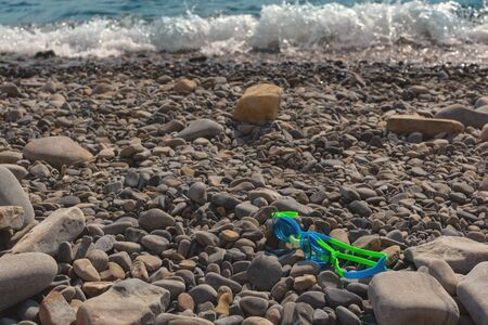 Beach vacation by the sea on a pebble beach. Ochki blue-green for swimming lie on the gray stones on the beach.の写真素材