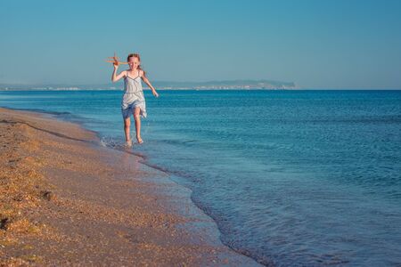 Beautiful red-haired girl, playing with a toy airplane, runs along the sandy beach of the sea against the blue summer sky and enjoys the rays of the sun and freedom.
の写真素材