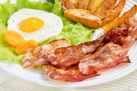 
Fried bacon with French fries and a delicate egg, close-up.の写真素材