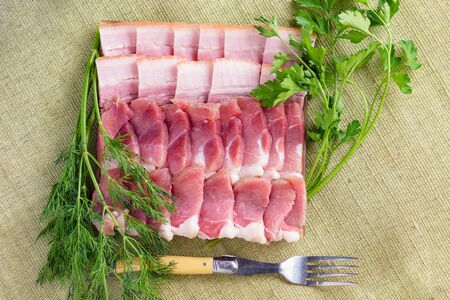  Sliced bacon with dill and parsley. Still life of bacon and greens. Bacon slices close-up.  On natural background lies bacon slices, greens and fork.の写真素材
