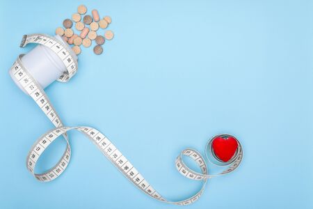 White jar of medications wrapped in a flexible ruler for fitness.Blue background with heart and copy space.Concept of losing weight when taking BIO supplements. Healthy lifestyle.の写真素材