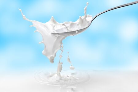 Milk splash in a spoon with milk against the blue sky with clouds.Beautiful splash of milk on the background of gentle clouds.の写真素材