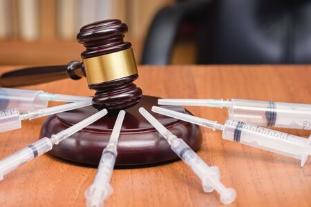 Judge's gavel and syringes on a wooden table. The concept of the fight against drugs and drug addiction. Court hearing against drugs. Medicine and law.の写真素材