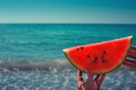 Watermelon, juicy, red slice in the hands of a woman against the background of the ocean, in the...