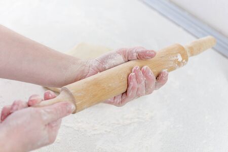 Female hands are holding rolling pin sprinkled with flour.