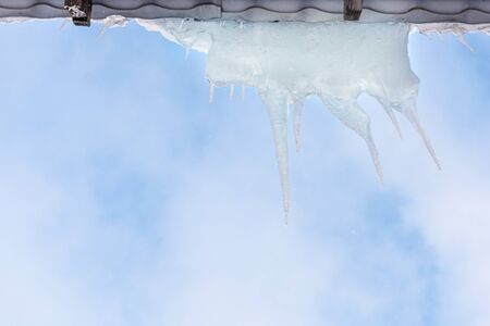 Long icicles against blue sky. Winter, icicles, ice on the roof. Icicles. Icicles hang on the roofs of house in winter. の写真素材