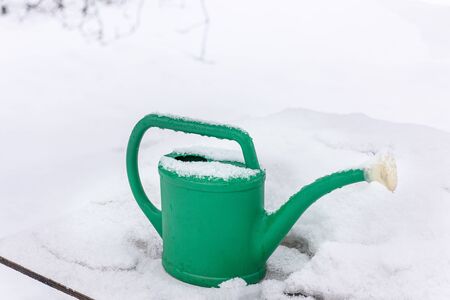 Snow, frost, snowflakes are falling. Watering can garden in the snow in the winter in the garden. A snow-covered garden watering can. Garden tools in winter in the snow during the day. の写真素材