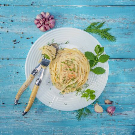 Dish standing on a blue wooden table, a plate with Italian pasta and chicken with a sauce of Provencal herbs, decorated with herbs, salt and garlic.の写真素材