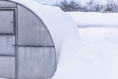 Winter, snow, frost in the garden. Greenhouse in the snow. Snow-covered greenhouse. Lot snow on the roof greenhouse. の写真素材