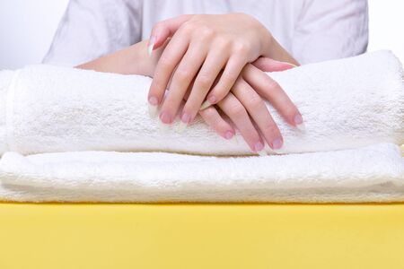 Beautiful hands of young woman close-up on towel. Spa treatments for nails. Space for text. Woman holds hands on towel for manicure treatment procedure in spa salon. の写真素材