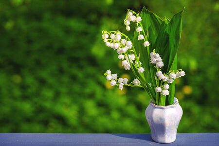 Bouquet of spring flowers standing in a vase on a wooden table with copy space.Lily of the valley. Flower Spring Sun White Green Background Horizontal. Ecological background Blooming lily of the valley on green grass background in the sunlight. Spring flower lily of the valley.の写真素材