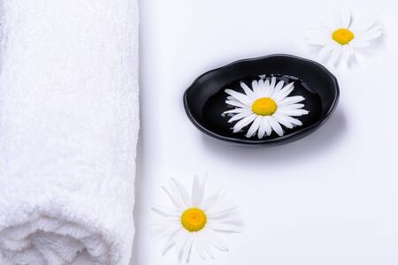 Spa treatment concept with terry towel and black plate with liquid in which white daisy floats. Natural oils for SPA.の写真素材