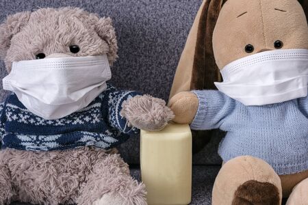 Means of protection against the virus soap and mask. Wash hands with soap after talking to each other. Bear and bunny are sitting on a sofa in protective medical mask. Protective mask protects against coronvirus and the flu epidemic.の写真素材