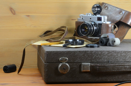 An old film camera lies on a suitcase with a photographic enlarger, on a wooden background.の写真素材