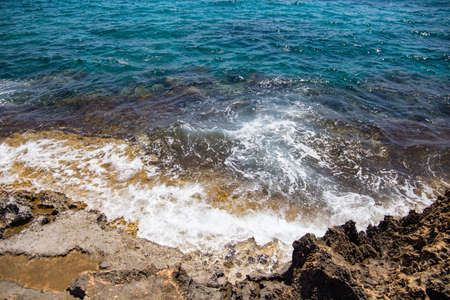 a rocky seashore against the background of water and sky washed by a blue wave at the cliffの写真素材