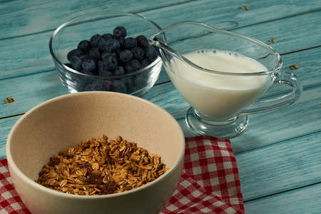 The bowl of granola, blueberries and cup of milk on the blue wooden background.の写真素材
