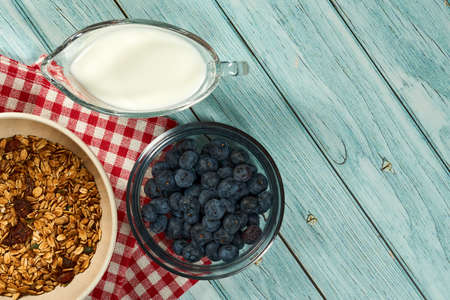 The bowl of granola, blueberries and cup of milk on the blue wooden background.の写真素材