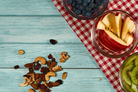 Three cups of blueberry, apple and kiwi with some nuts on the blue wooden background.の写真素材