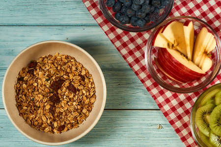 Three cups of blueberry, apple and kiwi with some nuts on the blue wooden background.  Cup of granola on the left side.の写真素材