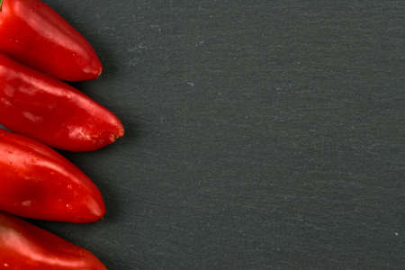 Red small Bulgarian peppers(Bell pepper) with drops of water on them on a black stone table. Wooden background, flatlay. There is space for text on a side.の写真素材