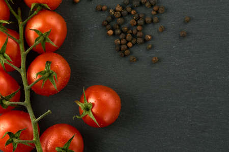 Cherry tomatoes on a black stone table flatlay. Image can be used as a texture as well. Some pepper on the right side.の写真素材