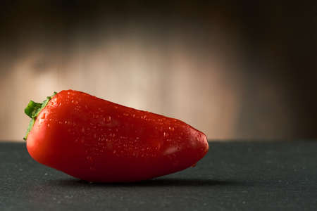 Red small Bulgarian pepper(Bell pepper) with drops of water on it on a black stone table. Wooden background.の写真素材