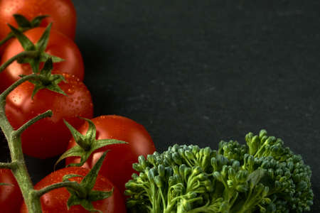 Cherry tomatoes and small broccoli on a black stone table. Image can be used as a texture as well, I left some space for the text on the right side.の写真素材