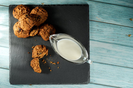 Chocolate cookies with raisins and cup of milk on a black plate. Top view, flatlay.の写真素材