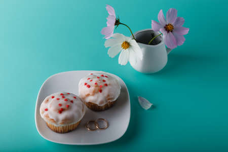 Colorful muffin on saucer with flower. Aqua color background and wedding ringの写真素材
