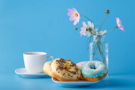Concept beakfat. Donuts on saucer with cup of tea and flowers