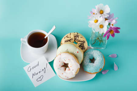 Four donuts on saucer with cup of tea. Aquamarine backgroundの写真素材