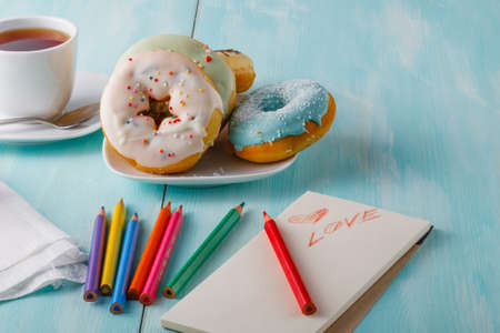 olorful donuts on saucer and sketchbook with painted heartの写真素材