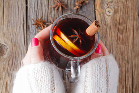 Hot mulled wine in female hands, spices on weathered wooden table. Sweethome conceptの写真素材