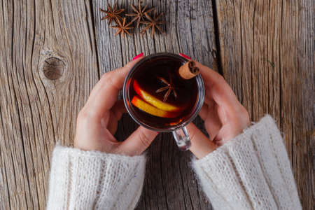 Hot mulled wine in female hands, spices on weathered wooden table. Sweethome conceptの写真素材