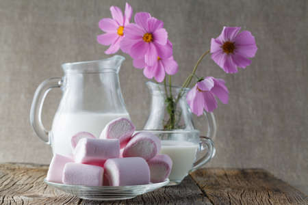 colored mashmallow with milk on wooden table with flowersの写真素材