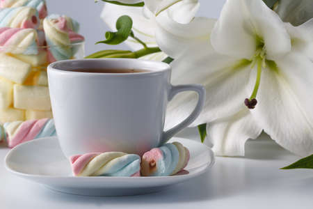 Breakfast concept. Cup of tea, white lily and colored marshmallowの写真素材