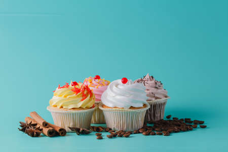 Four colorful pink cupcake on aquamarine background with cinnamon stick and coffee