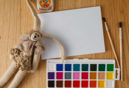 Kid painting concept. Paints with brush on table with felt cozy dollの写真素材